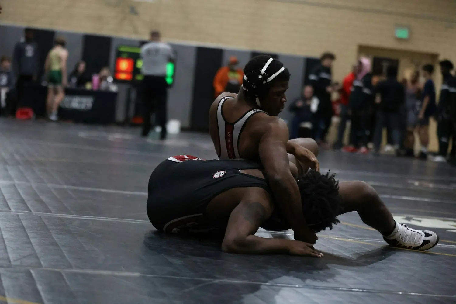 Two wrestlers compete on a mat during a dual, one riding behind the other.